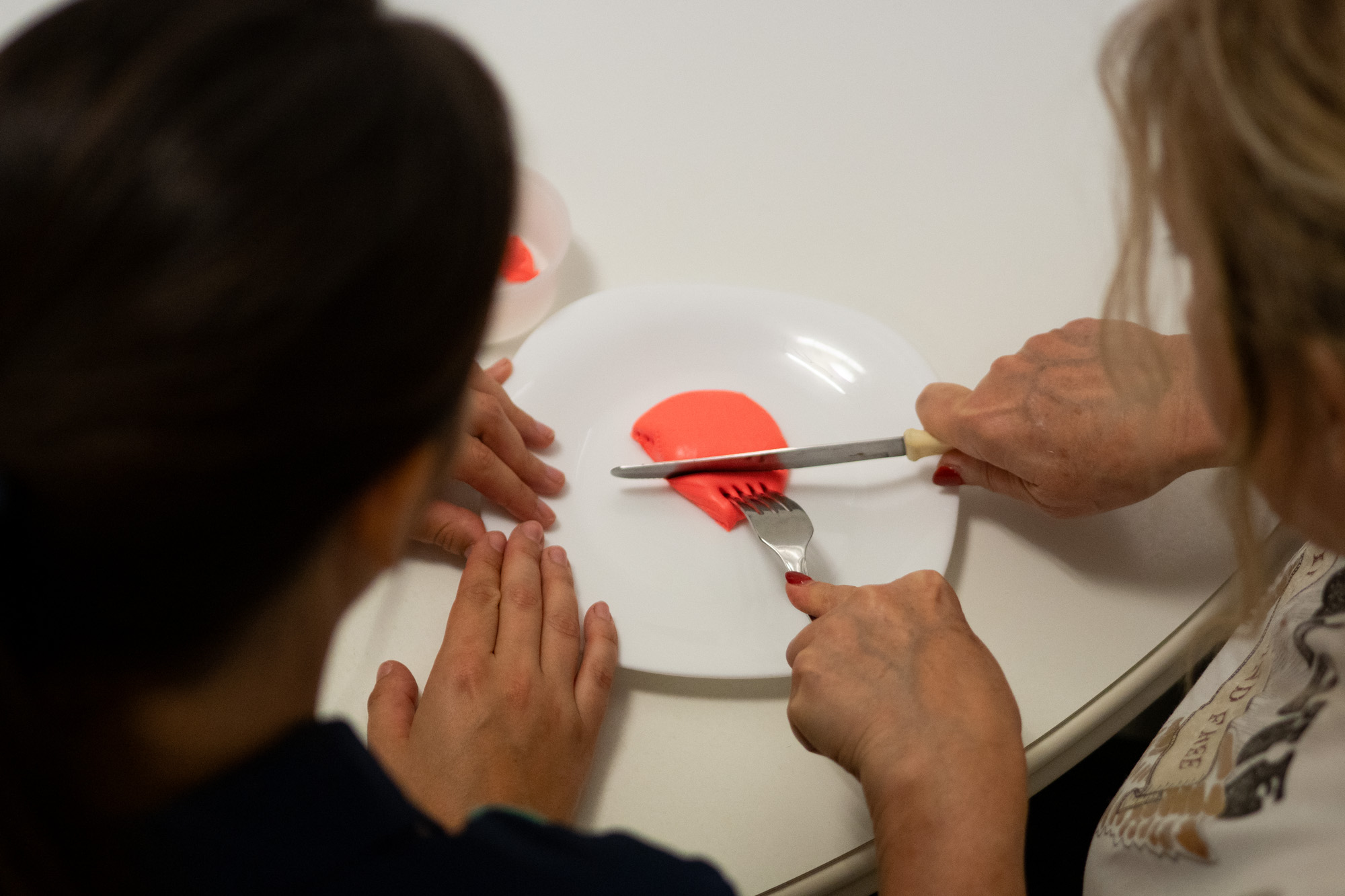 Persona practicando el uso coordinado de cuchillo y tenedor durante una sesión de terapia ocupacional a domicilio